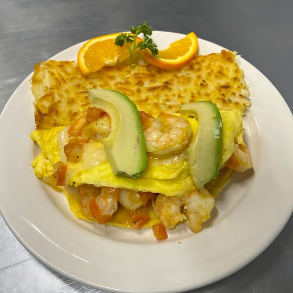 Shrimp and avocado omelet with hash browns, garnished with orange slices and parsley.