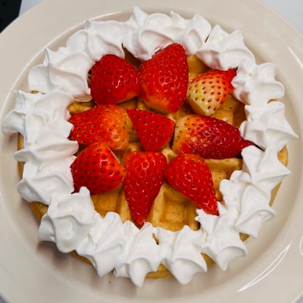 A golden waffle topped with fresh strawberries and a generous swirl of whipped cream on a white plate.