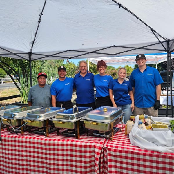 Six Santana's Cottage Cafe staff members in blue shirts stand behind a red and white checkered buffet table.
