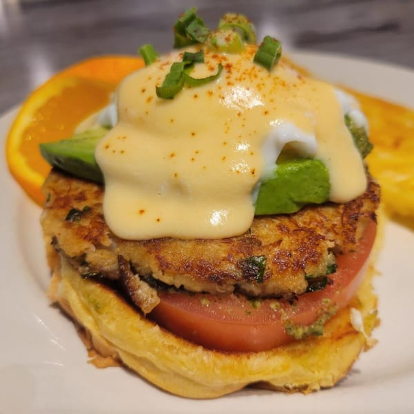 Santanas Cottage Cafe's crab cake benedict with avocado, hollandaise, and scallions, served with an orange slice.
