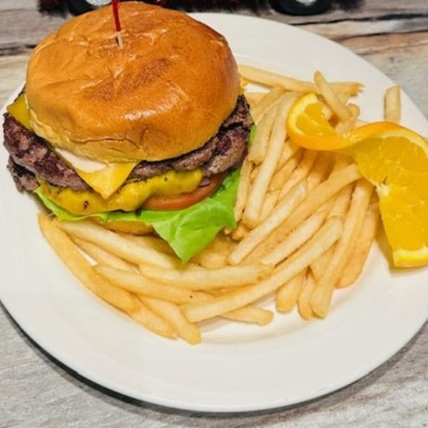 A double cheeseburger with lettuce, tomato, and pickles, served with french fries and orange slices.