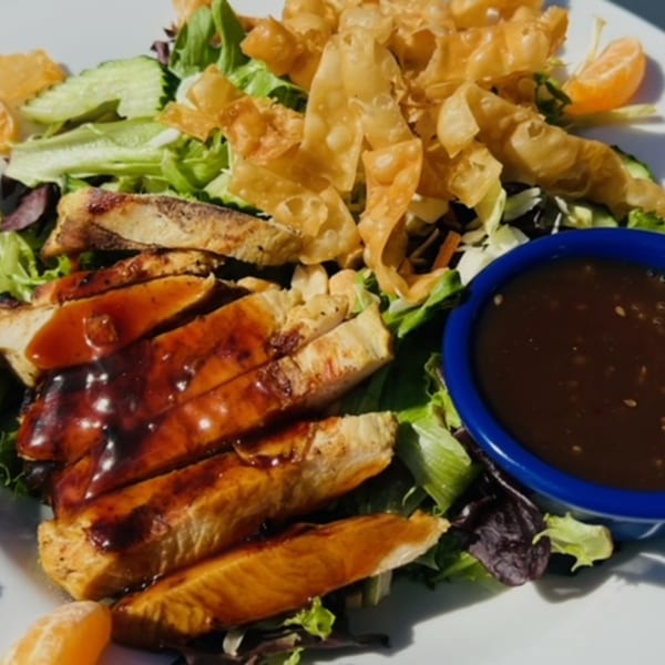 Grilled chicken salad with crispy wontons, mandarin oranges, and a side of dressing.