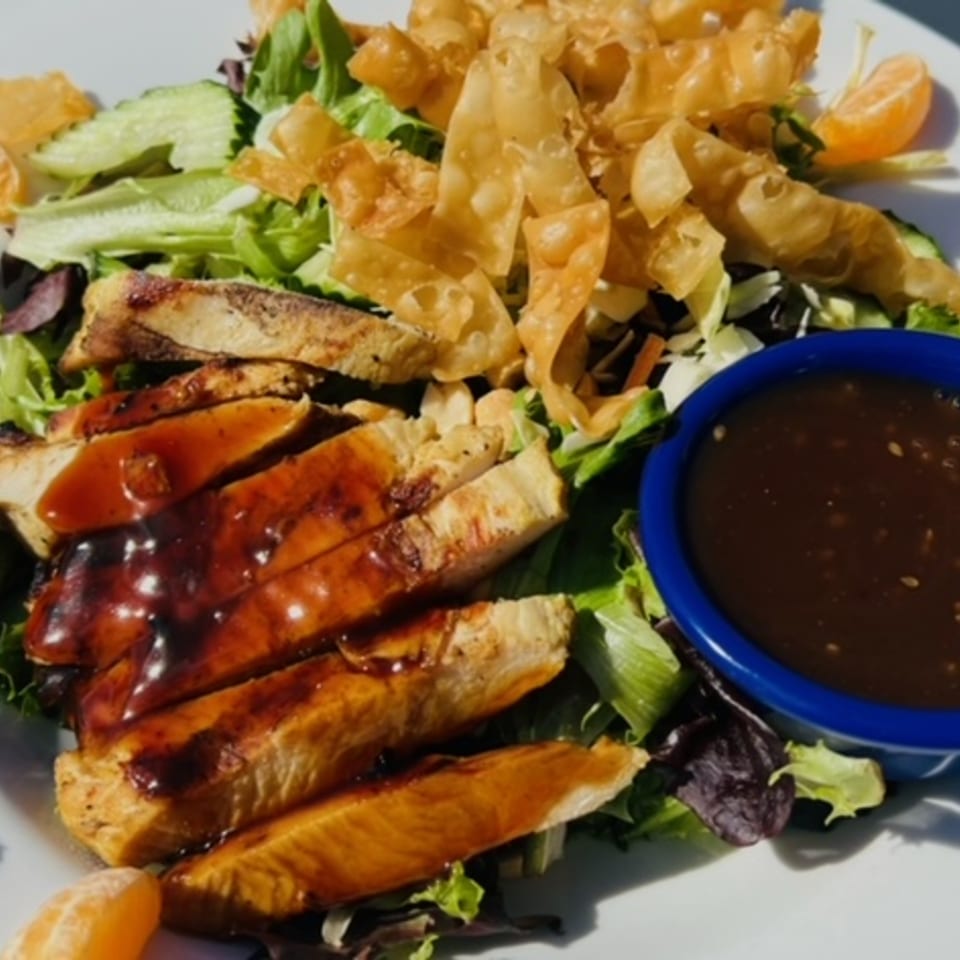 Grilled chicken salad with crispy wontons, mandarin oranges, and a side of dressing.
